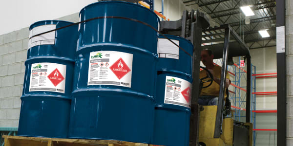 4 large chemical drums of acetone are being transported on a forklift. The big blue drums are labeled with Avery 60501 UltraDuty GHS labels indicating the contents are flammable.