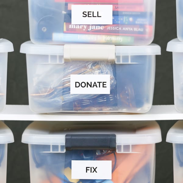 Three plastic bins stacked on shelving. Each bin is labeled with Avery 6465 label to help declutter a home. The labels read, "Sell," "Donate," and "Fix,"