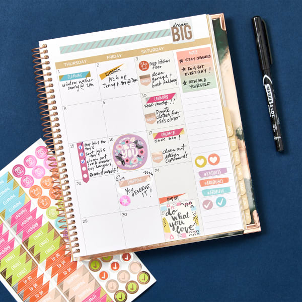 A planner opened to a calendar page with decluttering goals noted using Avery planner sticker pack 6780.