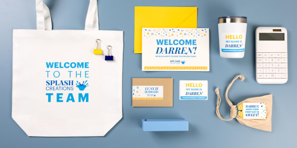 The contents of an onboarding kit laid out on a blue table next to a customized tote bag. The kit items have been personalized with Avery labels, cards, and tags.