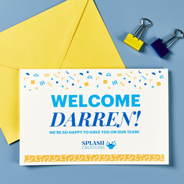 An onboarding kit welcome card printed on Avery greeting card 3378. The card is shown with a yellow envelope and office supplies arranged on a blue table. 