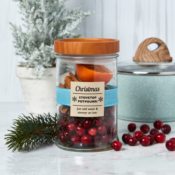 Cozy Christmas-in-a-jar gift idea showing an example of stovetop potpourri mix. You can see cranberries, cinnamon sticks and half an orange right off the bat. The jar is decorated with Avery square Kraft paper labels 22846.