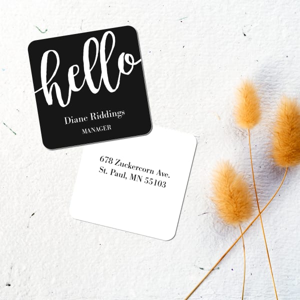Graphic black and white square business card design with "hello" in a large looping handwritten font. The design is printed on Avery business card 35702 and shown on a cool textured surface with fuzzy mustard-yellow plant.