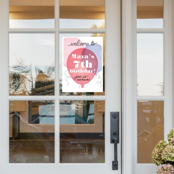 A glass front door with an adhesive sign that reads, "Welcome to Maya's 7th Birthday! Join us out back!" The sign features balloons in a soft, modern color palette and is printed on Avery 61512 decal sheets.
