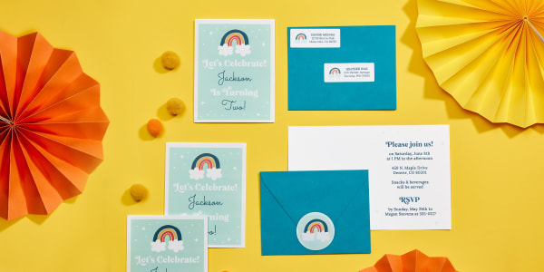 DIY birthday invitations with coordinating envelope seals and address labels are shown decoratively laid out on a bright yellow background. The invitations are made with Avery 8315 printable note cards and a free Avery template with a cute retro rainbow design. The matching address labels are printed on Avery 5160 labels, and the matching envelope seals are printed on Avery 22807 round labels.