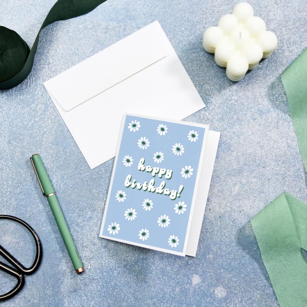 This image is an example of a birthday invitation made with Avery 8315 note cards and a customizable Avery template. The template has a light blue background with white daisies and white text. The daisies have green centers, and the text has a green highlight.
