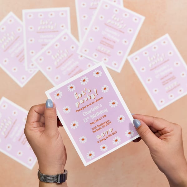 The image shows an example of birthday invitations printed on Avery 8387 postcards. The design of the invitations is a free Avery template featuring white daisies and text accented in orange on a light pink background.