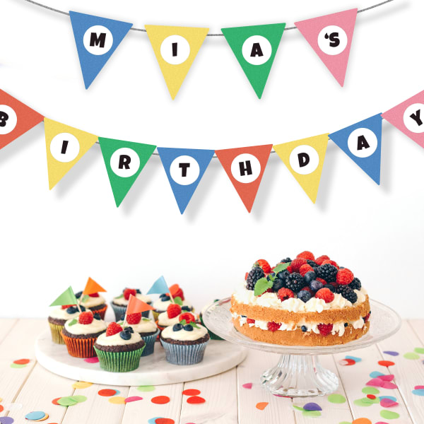 Berry cupcakes and a berry cake are displayed on a table with a birthday banner strung up on the wall. The simple, colorful bunting has Avery 22807 labels applied that spell out Mia's Birthday.