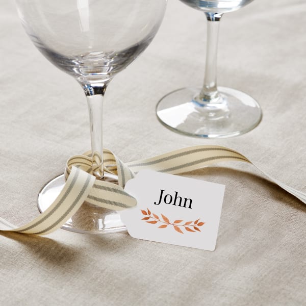A simple wine glass tag made with Avery 22848 scalloped-edge tags. It's shown tied to a wine glass stem with elegant cream and grey striped ribbon. 