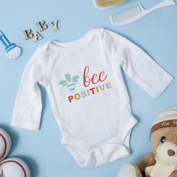 Image showing a white onesie with a colorful baby onesie template that reads “bee positive.” 