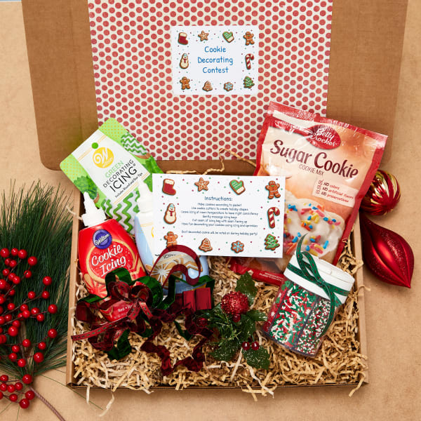 A cookie decorating kit for a virtual holiday party is neatly packaged in a cardboard mailer. There's sugar cookie mix, different icings, sprinkles and cookie cutters along with instructions printed on Avery postcard 5389.