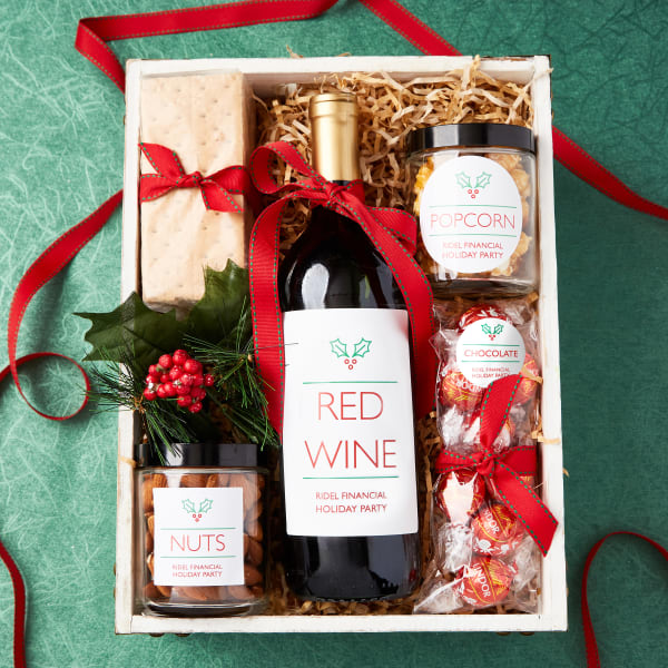 Virtual holiday party wine and snack box idea. Nuts, wine, popcorn and chocolate are personalized with Avery labels and packed neatly in a box for shipping.