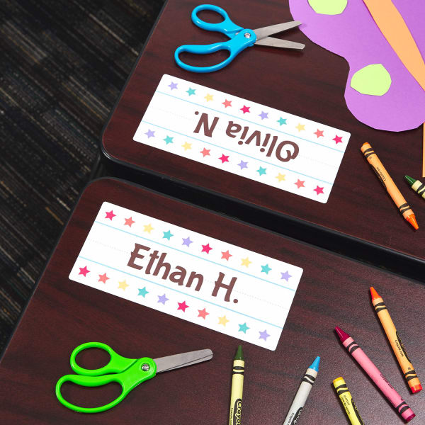 student desks with name labels and colorful school supplies