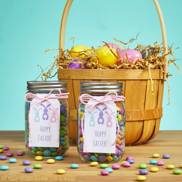 A Mason jar filled with pastel candy and decorated with a "Happy Easter" tag is shown as an example of DIY Easter party favors. Avery 22802 tag is printed with bunny graphics and reads, "Hoppy Easter."