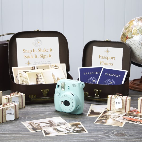 Two decorative mini trunks are set up with a globe on a wooden desk. There is an instant camera and supplies to make "passport" photo books for a travel party themes. Avery cards are used for the passport books and Avery Surface Safe signs decorate the inside of the trunks.