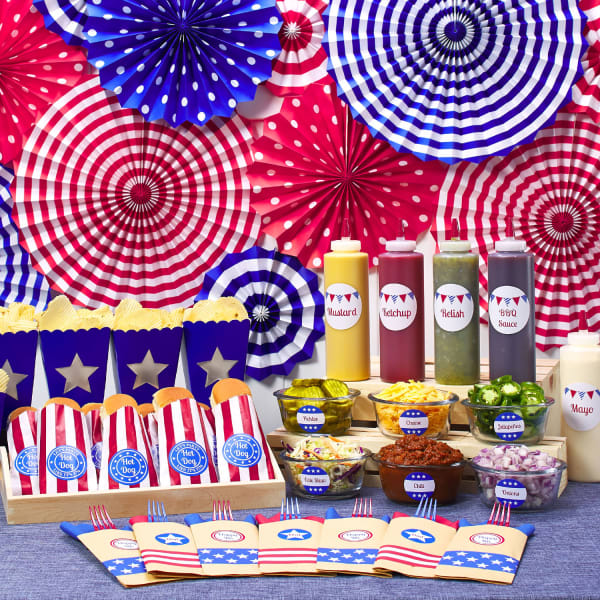 A hot dog bar display for a 4th of July party idea. Buffet food and condiments are labeled with personalized red, white, and blue Avery labels.