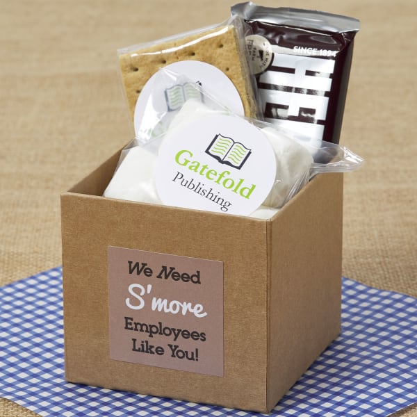 A cardboard box filled with ingredients to make s'mores, including graham crackers, a Hershey's chocolate bar and marshmallows. On the front of the box is a square Avery label 22816 that reads, "We Need S'more Employees Like You."