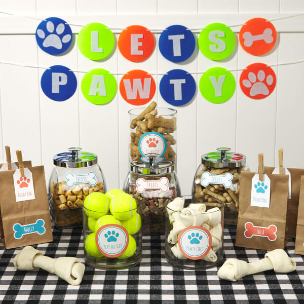 A table display for a dog birthday party. There are doggy bags and treat jars all personalized with Avery labels and tags. 