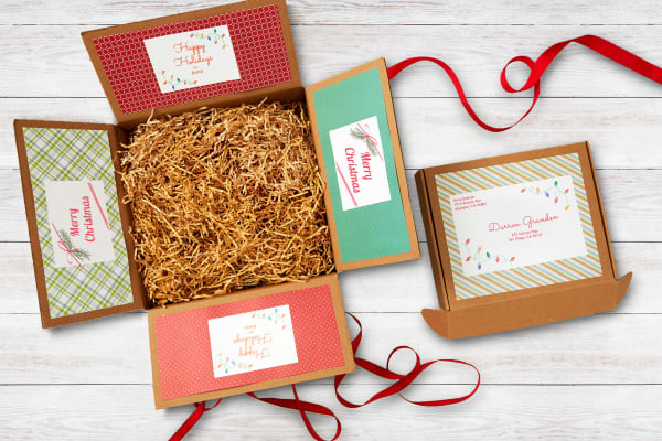 white wooden surface with open brown box filled with shredded shipping material and decorated with patterned holiday paper and labels next to closed brown box with custom avery shipping label