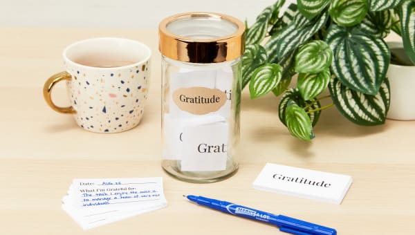 A glass gratitude jar filled with slips of paper with positive messages and appreciative thoughts sitting on a wood desk