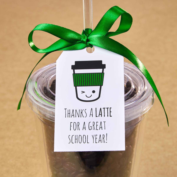 Cute DIY teacher gift idea for coffee lovers. A reusable iced coffee traveler filled with coffee beans to hide a Starbucks gift card inside. A git tag with a cartoon coffee cup character that reads, "Thanks a latte for a great school year!" is on the outside.
