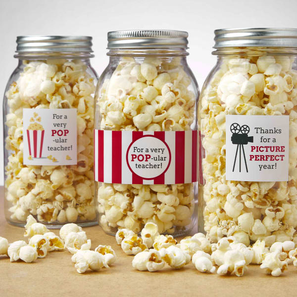 A Mason jar gift idea for teachers shows several jars filled with popcorn and labeled with a vintage movie popcorn-themed label. Two labels read, "For a very POP-ular teach," and the other reads "Thanks for a picture perfect year."