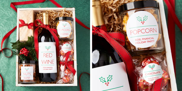 A wine and snack box gift with supplies for a virtual holiday party. A small wooden box is packed with wine, chocolate, popcorn and nuts decorated festively with personalized labels with Christmas holly accents.