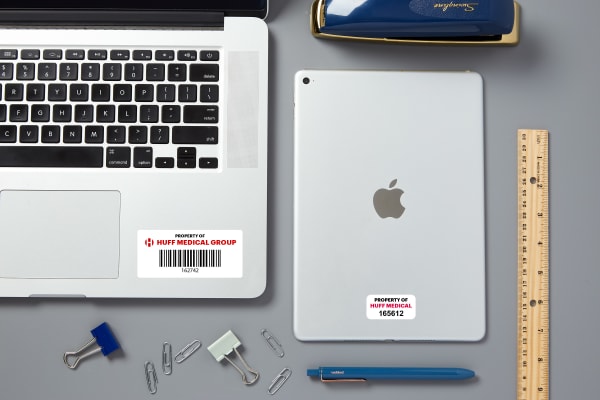 A laptop and a tablet labeled with Avery PermaTrack asset tags printed with barcodes.