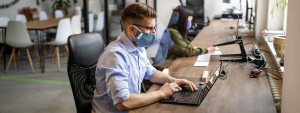 man sitting at desk laptop with face mask office open space