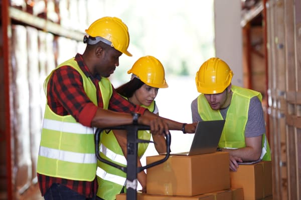 employees in an industrial facility checking inventory while wearing masks and hard hats