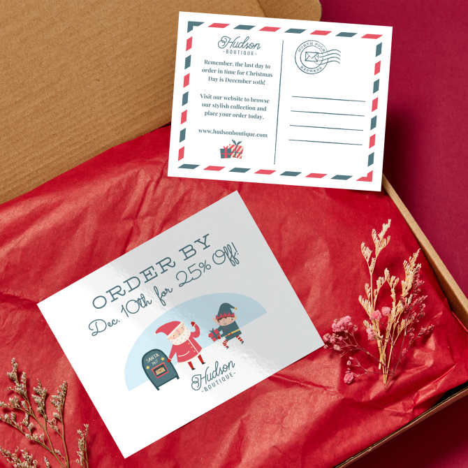 An Etsy packaging setup featuring a Christmas postcard. The back of the postcard is styled like an airmail envelope with space for a stamp and address so it can be mailed. The text features a reminder to order by December 10th to receive items in time for Christmas, along with the store's website link. The front of the postcard offers a 25% discount for orders placed by December 10th, illustrated with Santa Claus and an elf holding gifts. Both postcards are displayed on red tissue paper in a cardboard box, surrounded by dried flowers.