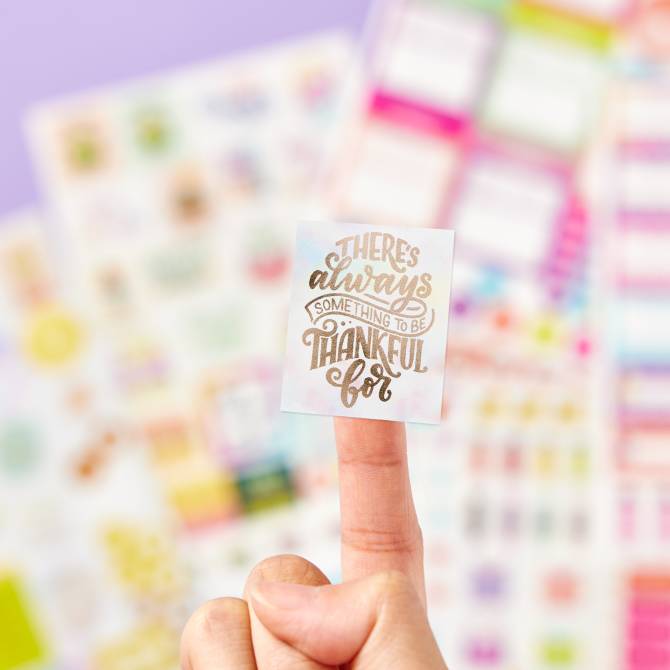 Avery 6785 planner sticker pack. One sticker with gold accents is shown up close and there are many more sheets from the pack in the background. 