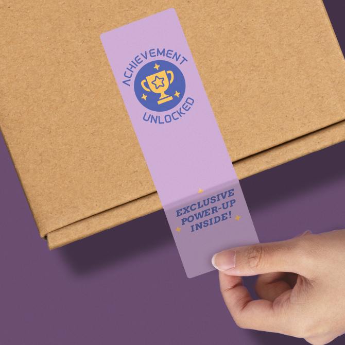 A hand placing a purple product packaging seal on a brown cardboard box. The seal features a trophy icon with the text 'ACHIEVEMENT UNLOCKED' above it and 'EXCLUSIVE POWER-UP INSIDE!' below it, all in a playful font with star accents.