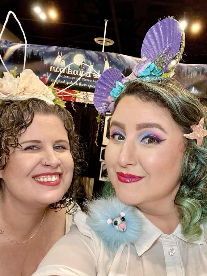 Two women wearing JoJo's So Creative headpieces and accessories take a selfie while working the brand's vendor booth at Ontario Comic Con Revolution.