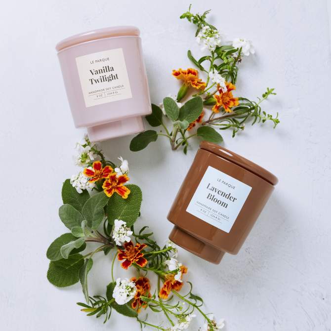 Image of two candles in pastel pink and brown jars labeled "Vanilla Twilight" and "Lavender Bloom" that are surrounded by small white and orange flowers. The candles showcase custom-designed Avery label templates great for farmers markets.