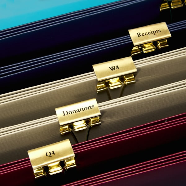 gold alligator clips with labels on the bottoms clipped face down onto blue, tan and red file folders on bright blue desk