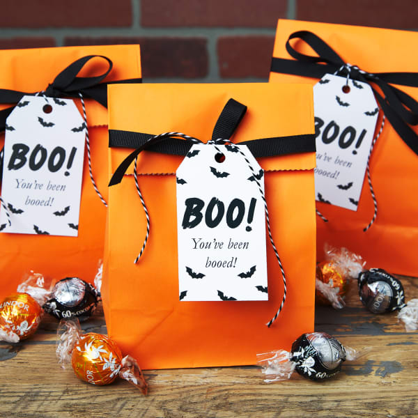 Bright orange "boo bags" with black ribbon and white tags, featuring the word "Boo!" in large letters and small black bats.