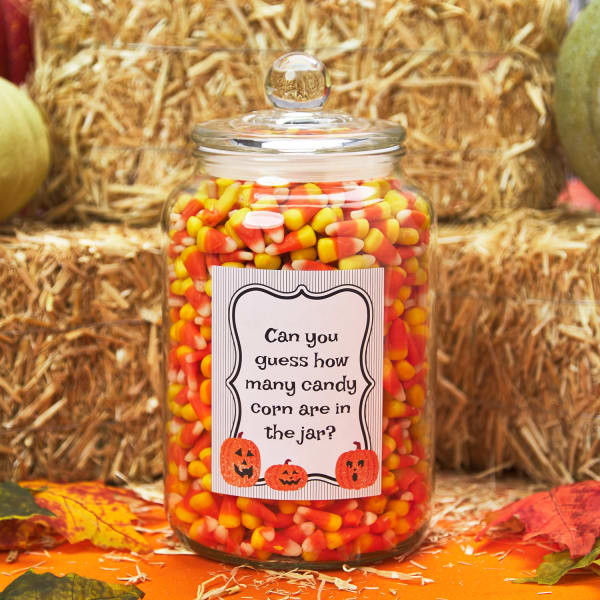 Large glass jar filled with candy corn featuring a large label with a Halloween themed party guessing game