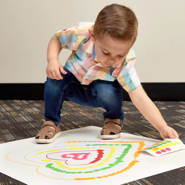 Toddler boy adding round stickers to heart shapes