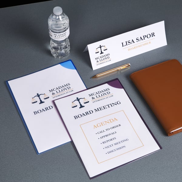 grey table with board meeting supplies including avery template tent card meeting agenda folder and water bottle