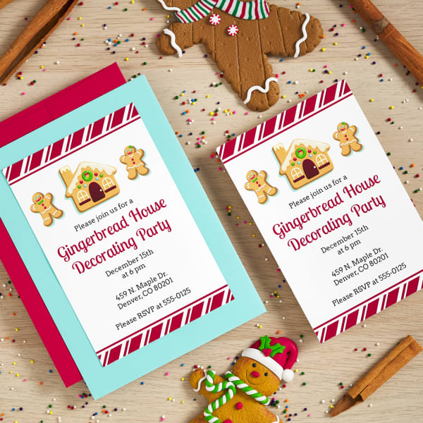 gingerbread house themed postcard invitations on top of colorful envelopes next to gingerbread people and cinnamon sticks