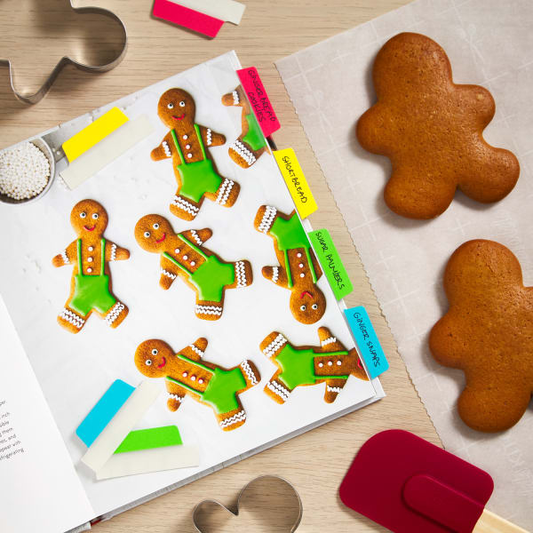 colorful margin tabs marking various pages of a holiday recipe book next to gingerbread men and cookie cutters