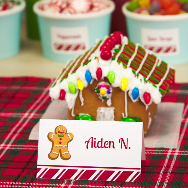 cute gingerbread house with colorful frosting and candy behind a gingerbread themed name card with the name Aiden N printed on