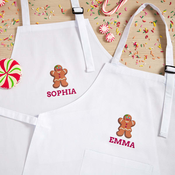 two white aprons with gingerbread person themed fabric transfer ironed on with individual guest names below