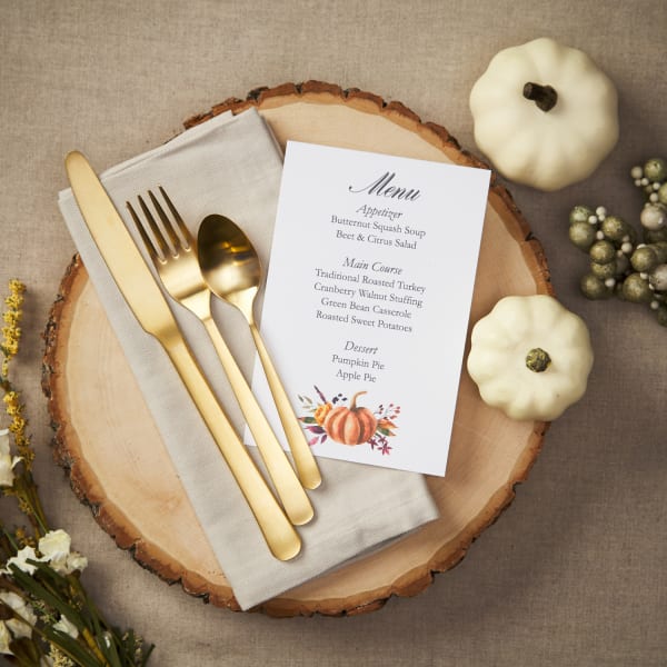 flatlay of gold cutlery on wood trunk cutout next to festive custom printed Thanksgiving menu