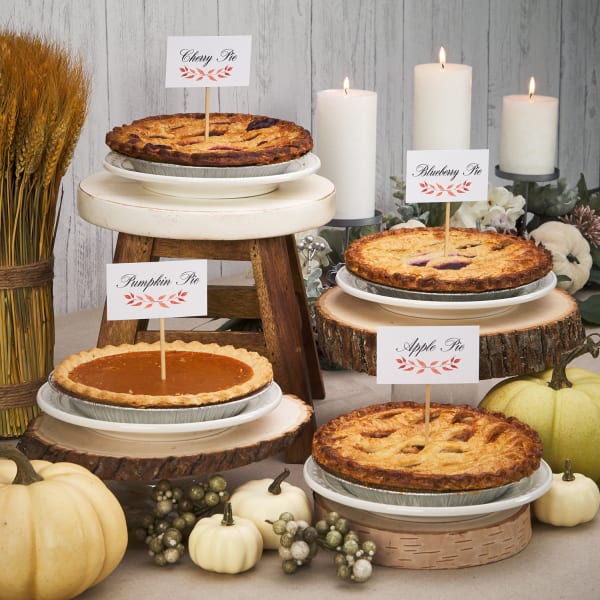 Thanksgiving themed pie tags on various pumpkin and apple pies on very festive Thanksgiving table filled with candles, pumpkins, and florals
