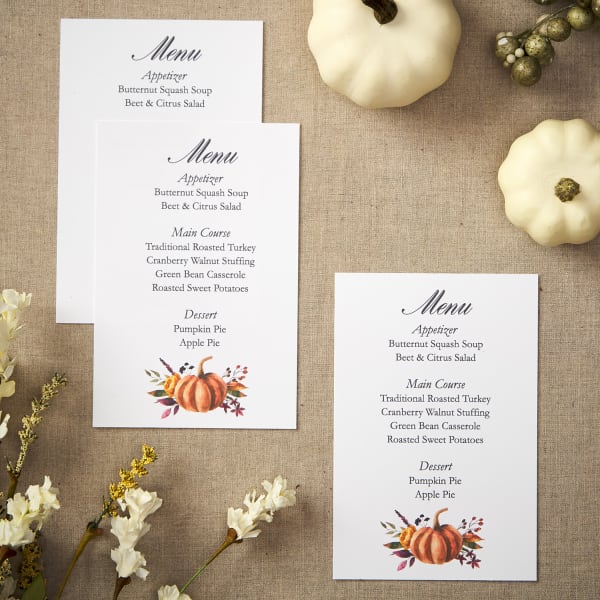 flatlay of three Thanksgiving menu cards next to white pumpkins and florals