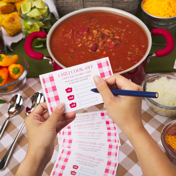 person filling out custom printed index cards with rules and tasting instructions, next to pot of chili