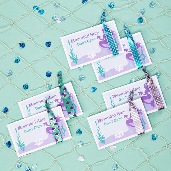 Avery 5388 index cards are personalized with a purple mermaid design that reads, "Mermaid Hair Don't Care." The party favors are completed with scale-print hair ties wrapped around the cards. 