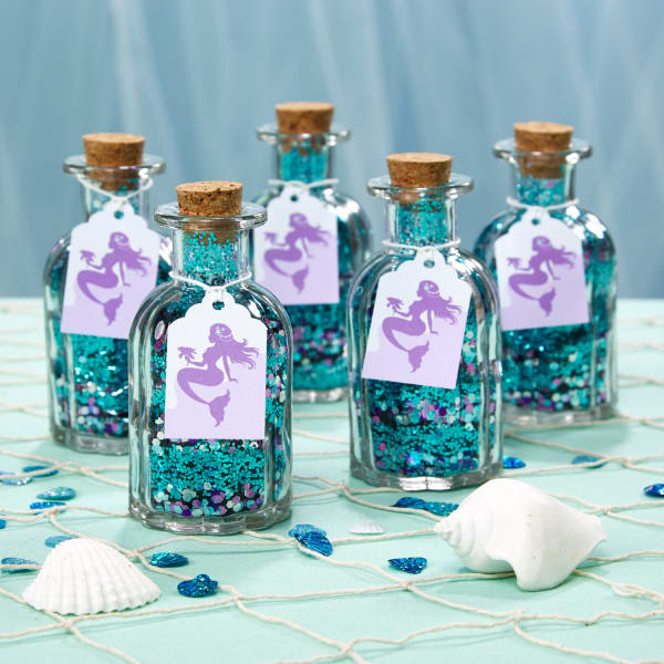 Small vintage-looking bottles with corks are filled with glitter to create a "mermaid tears" favor. The bottles are decorated with Avery 22848 tags printed with a purple mermaid design to emphasize the theme. 